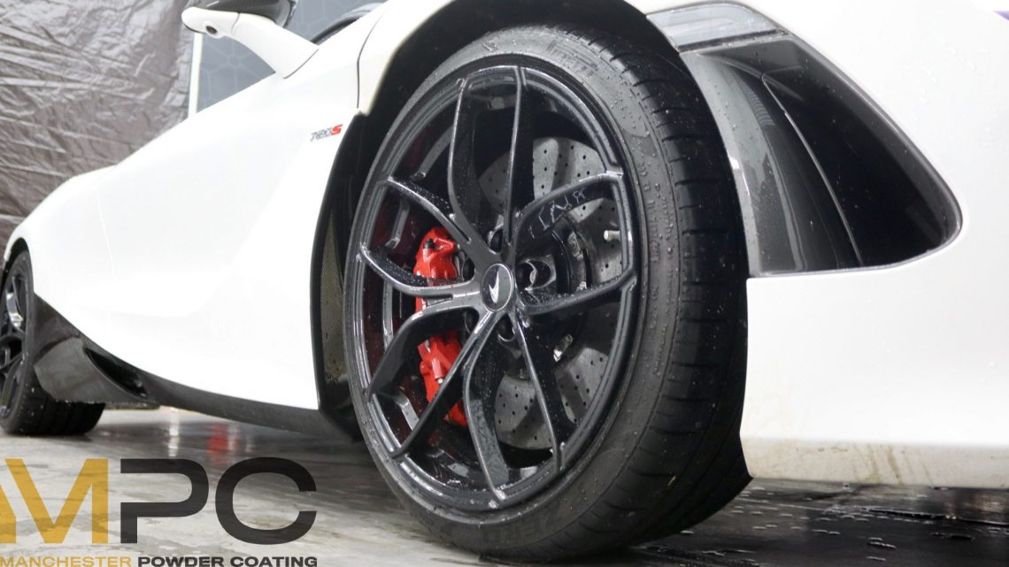 a McLaren wheel, refurbished to gloss black. It is a close up view of the wheel, with some of the white car visible either side.