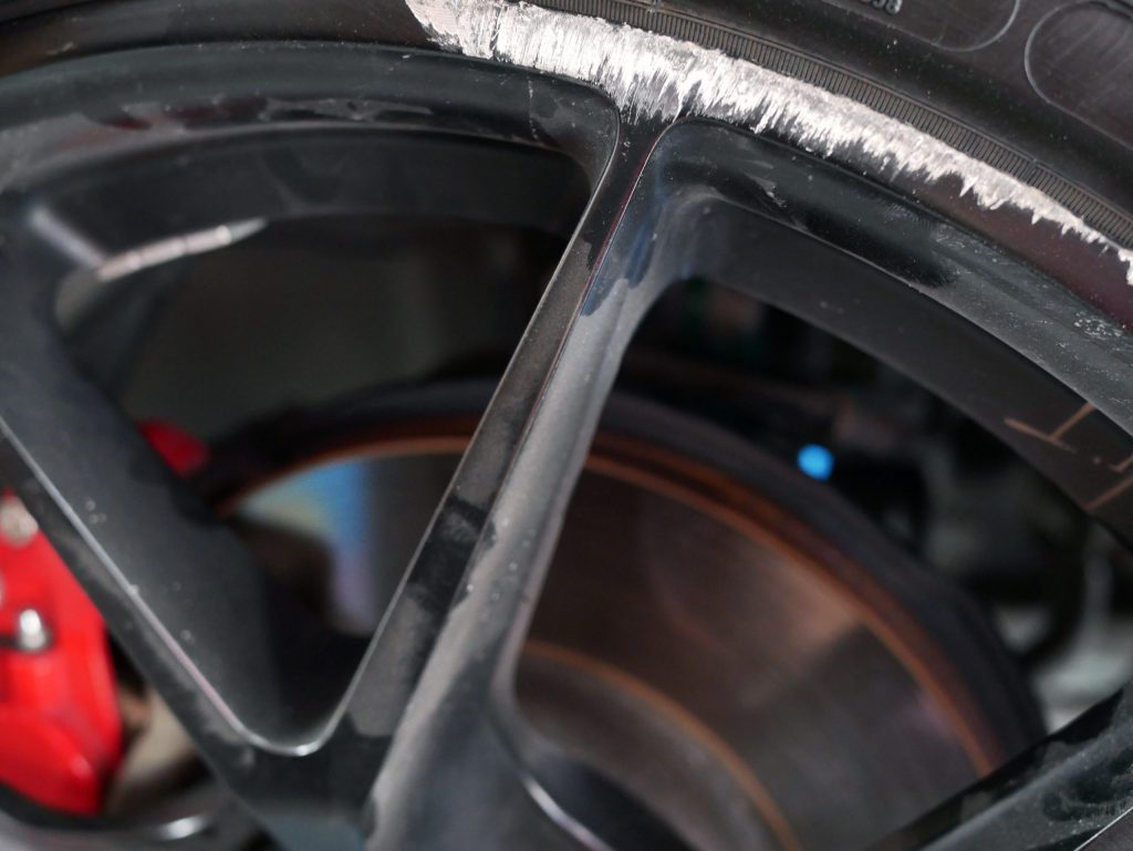 A close up of a kerbed wheel. The wheel is black, showing the silver of the alloy where it is damaged
