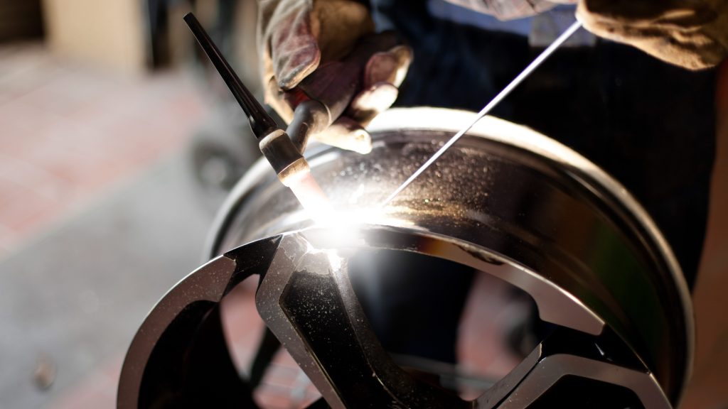 An image of a wheel being welded. You can only see the gloved hands of the welder, and half of the wheel.